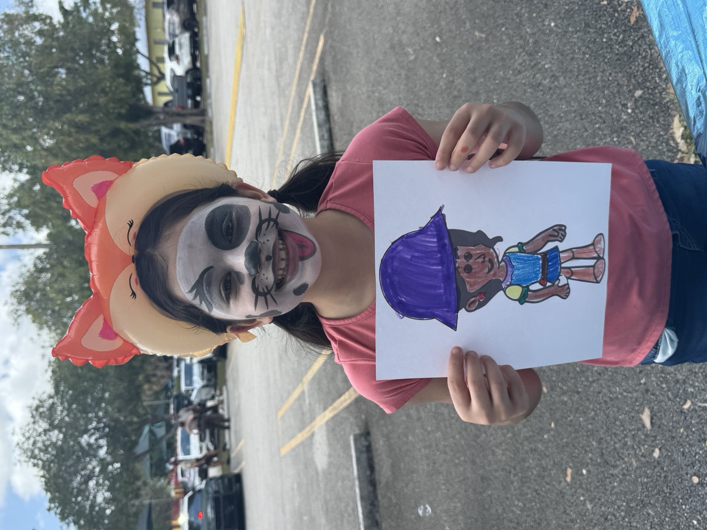 Girl with face paint holding her character artwork at event